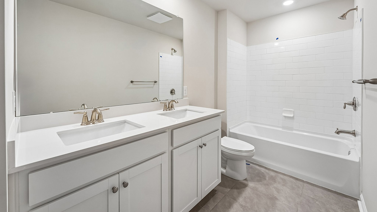 Secondary full bathroom in the Galen single-family home at Creekside Village featuring a dual-sink vanity, large mirror, tub and shower combination, and white subway tile surround.