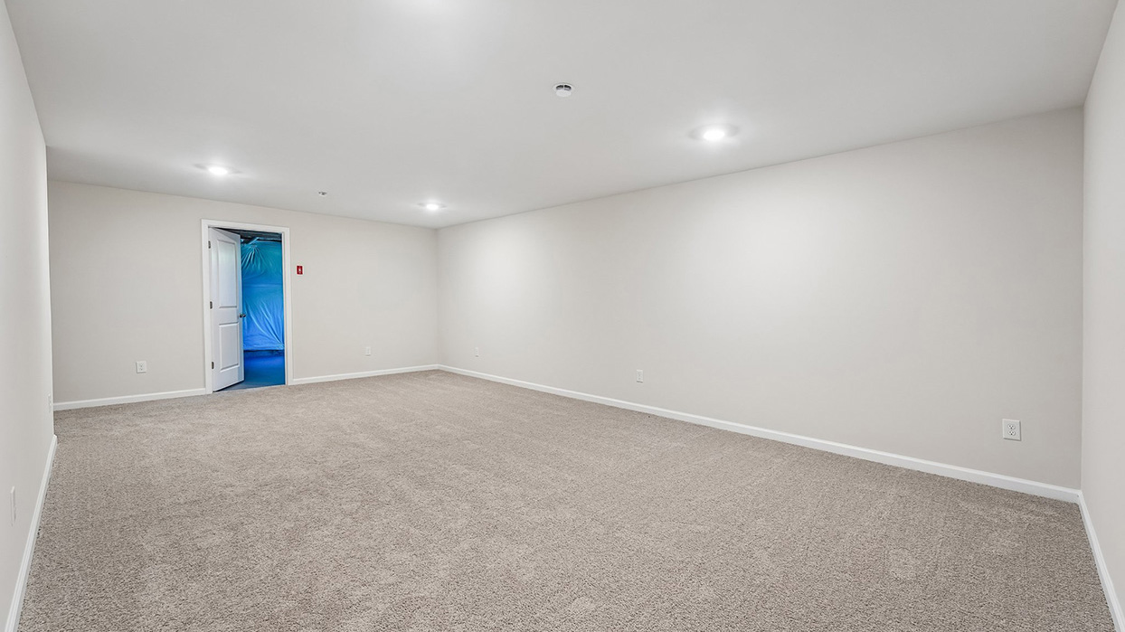 Finished lower-level recreation room in the Galen single-family home at Creekside Village featuring plush carpeting, recessed lighting, and flexible living space.