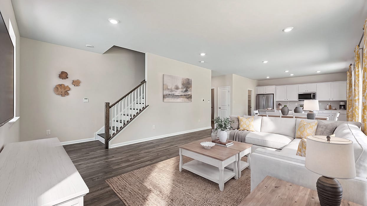 Open-concept main floor with staircase, wide plank flooring, recessed lighting, and kitchen visible in background