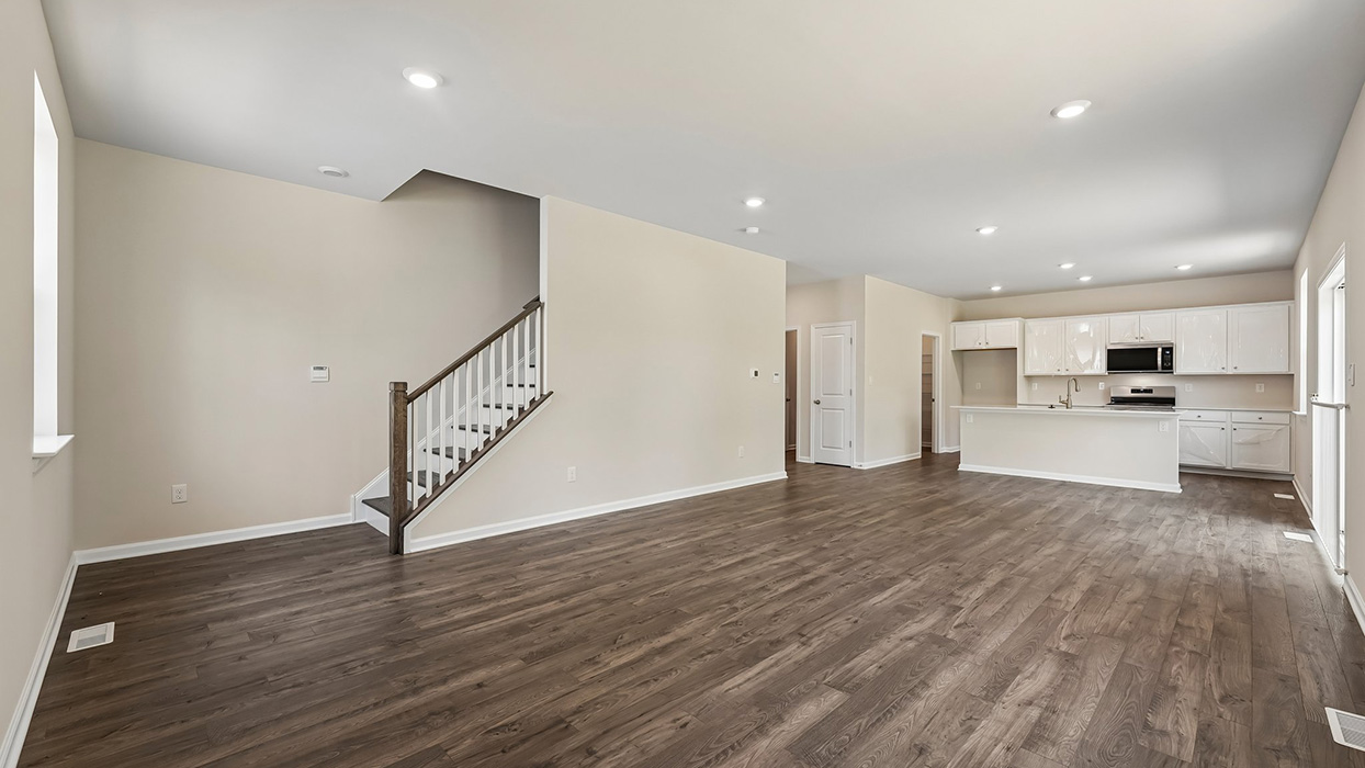 Open-concept main floor with staircase, wide plank flooring, recessed lighting, and kitchen visible in background