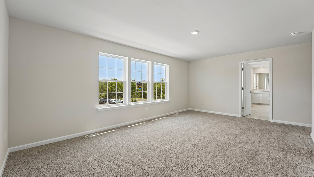 Owner’s suite with multiple windows, soft carpet flooring, and entry to private en-suite bathroom
