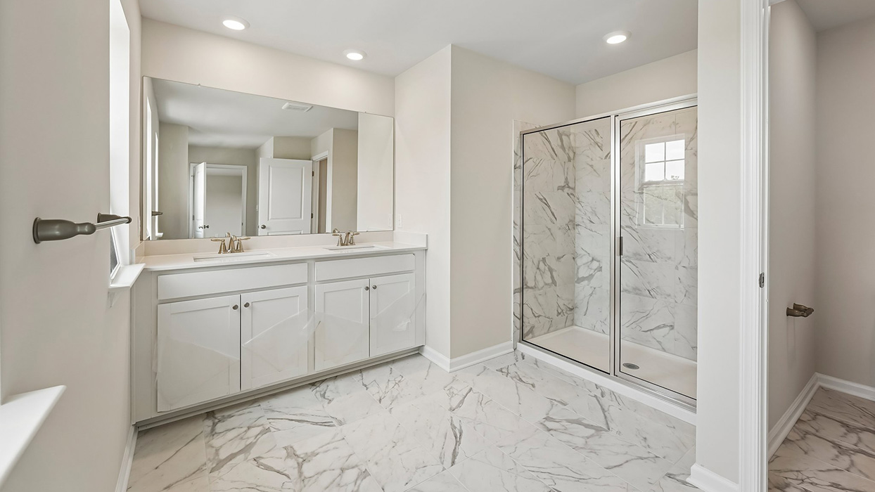Primary bathroom with dual vanity, large mirror, and glass-enclosed shower with tile surround