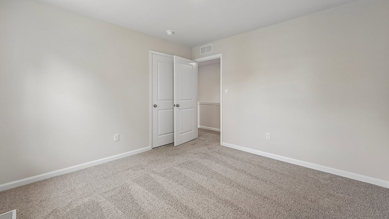 Secondary bedroom with neutral carpet, wide doorway, and access to hallway for convenient layout