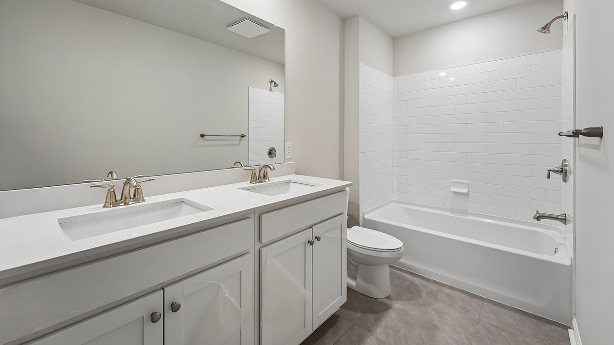 Full bathroom with double vanity sinks, large mirror, and tub shower with white tile surround