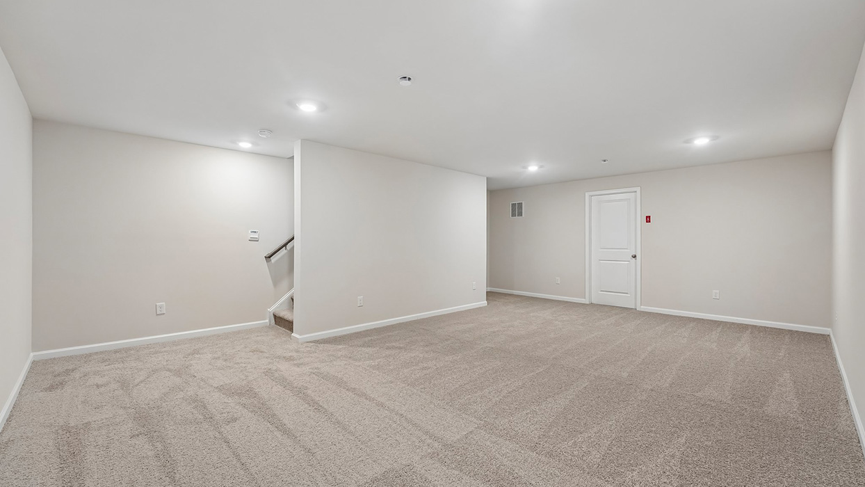 Spacious basement living area with carpet, recessed lighting, and stair access to main level