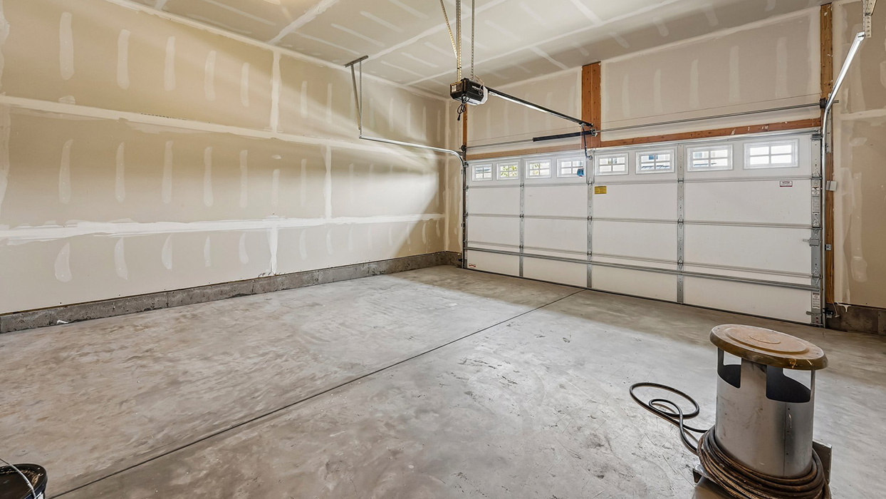 Garage interior with wide parking space, overhead doors, and additional storage area along walls