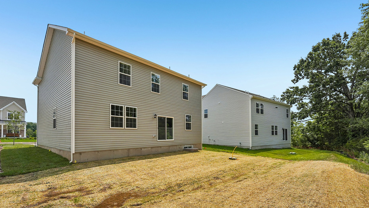 Angled rear exterior view of single-family home with vinyl siding, backyard space, and neighboring homes in Creekside Village