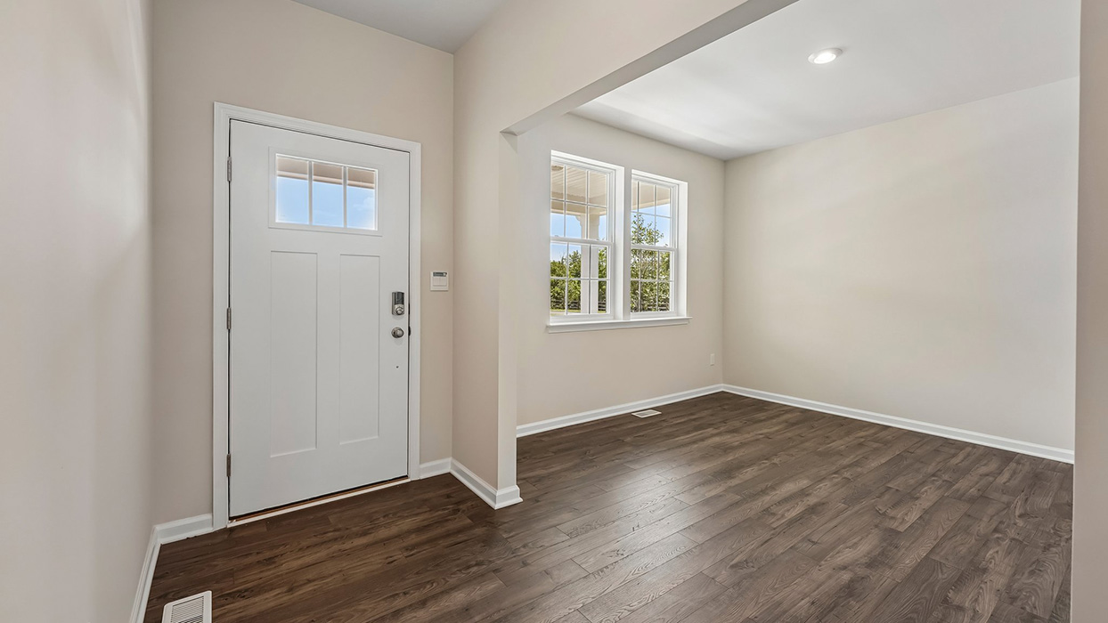 Entry foyer with natural light, front door window panel, and durable wood-look flooring leading into open-concept layout