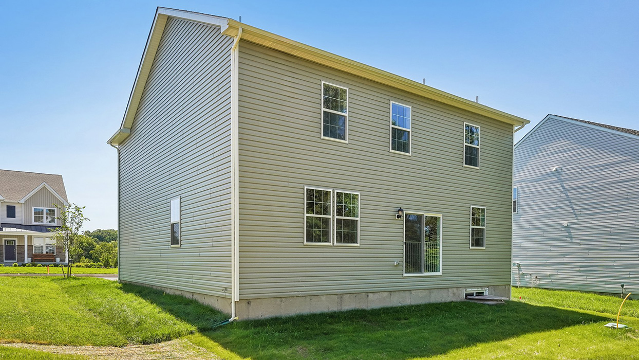 Angled rear exterior view of single-family home with vinyl siding, backyard space, and neighboring homes in Creekside Village