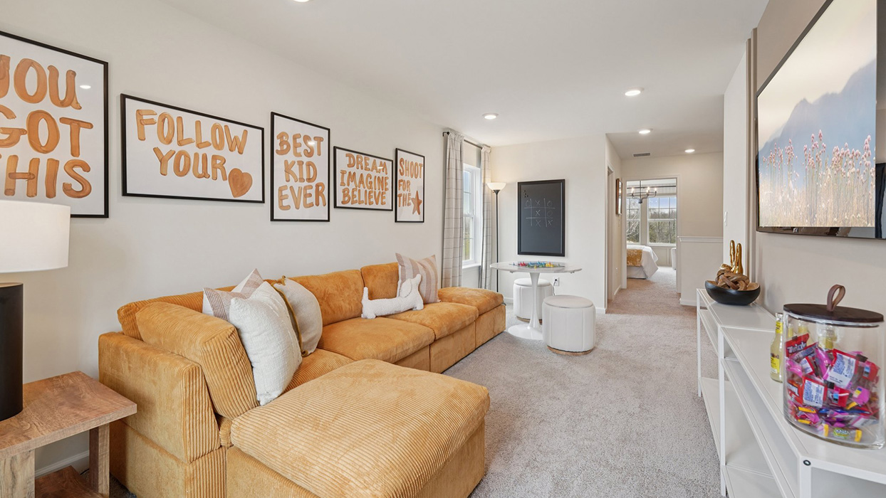The upstairs living with L-shaped couch facing a wall mounted TV.