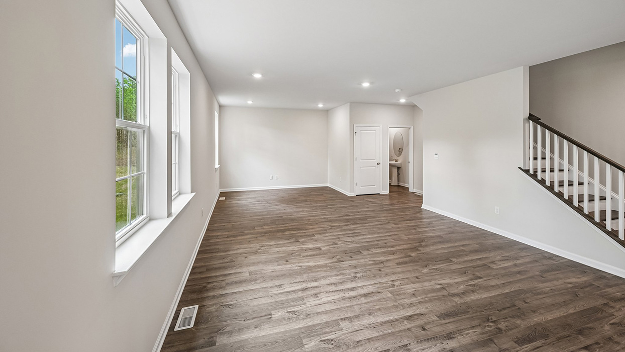 Open living area with wide plank flooring, staircase access, and view toward entry hallway