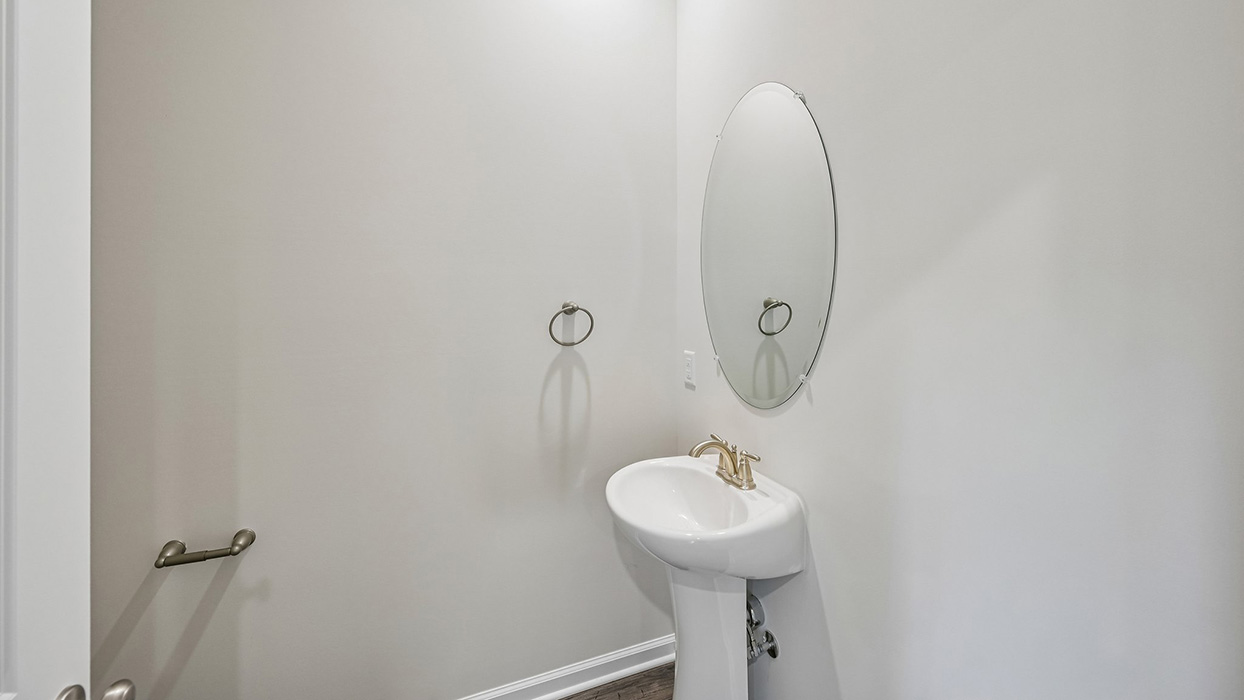 Powder room with pedestal sink, oval mirror, and neutral wall finish