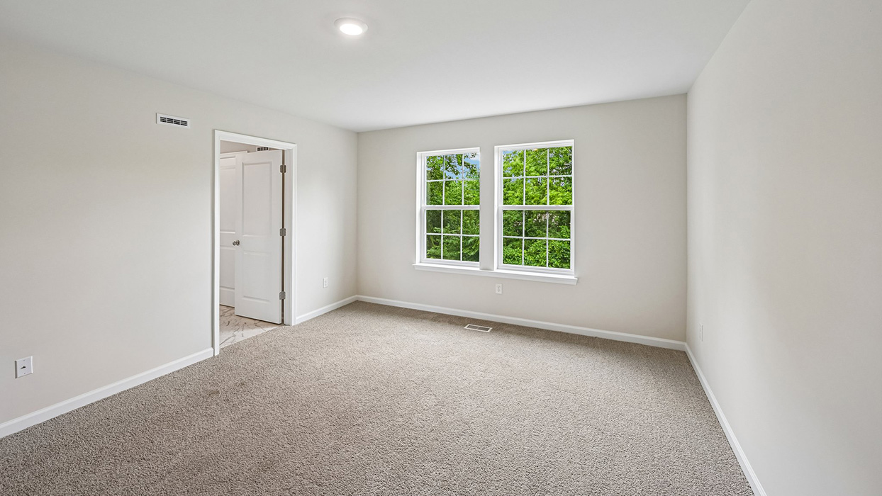 Primary bedroom featuring plush carpet, natural light from windows, and entry to ensuite bath