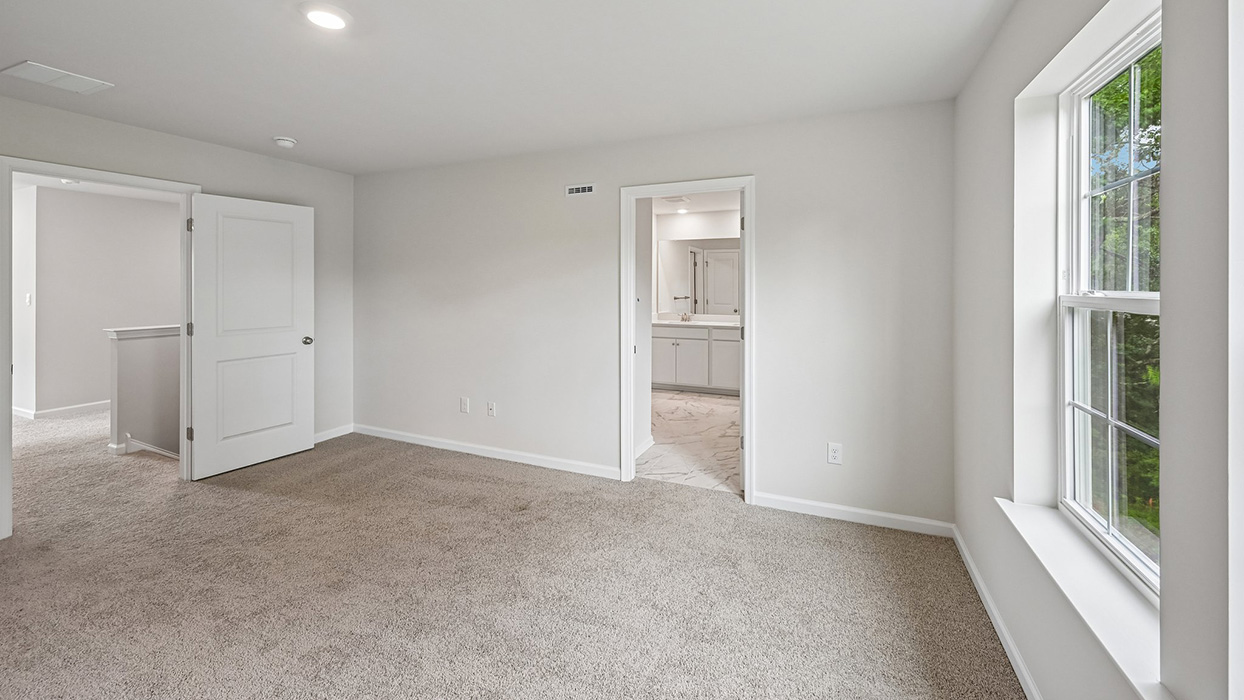 Primary bedroom with carpet flooring, natural light from window, and direct access to ensuite bathroom