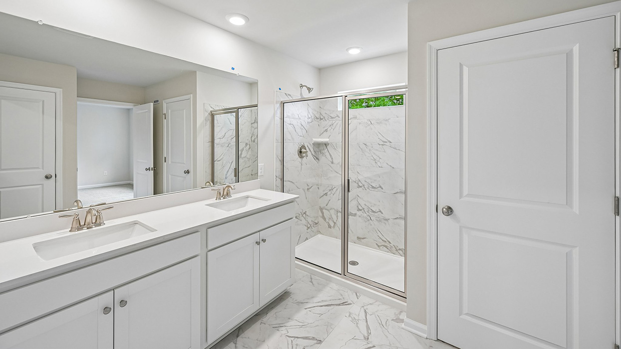 Primary bathroom with double vanity, large mirror, and glass-enclosed shower with tile surround