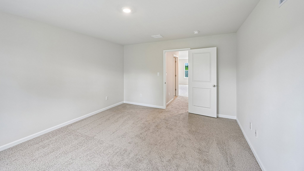 Secondary bedroom with plush carpet, neutral walls, and open doorway to hallway