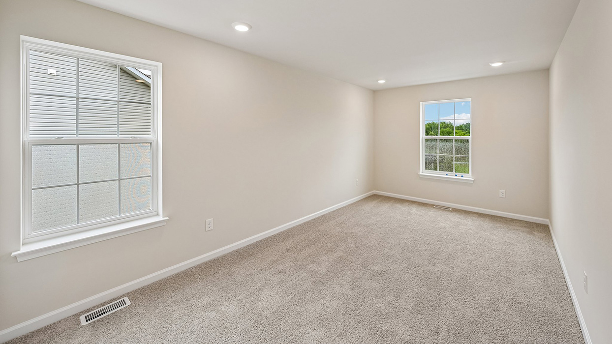 Secondary bedroom featuring dual windows, carpet flooring, and ample natural light