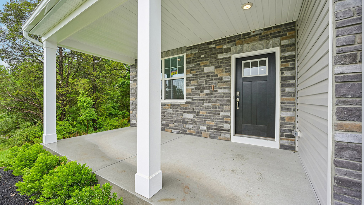 Covered front porch with stone exterior wall, black entry door, and concrete seating area