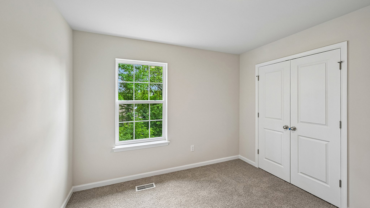Bedroom featuring double-door closet, plush carpet, and window with outdoor greenery views
