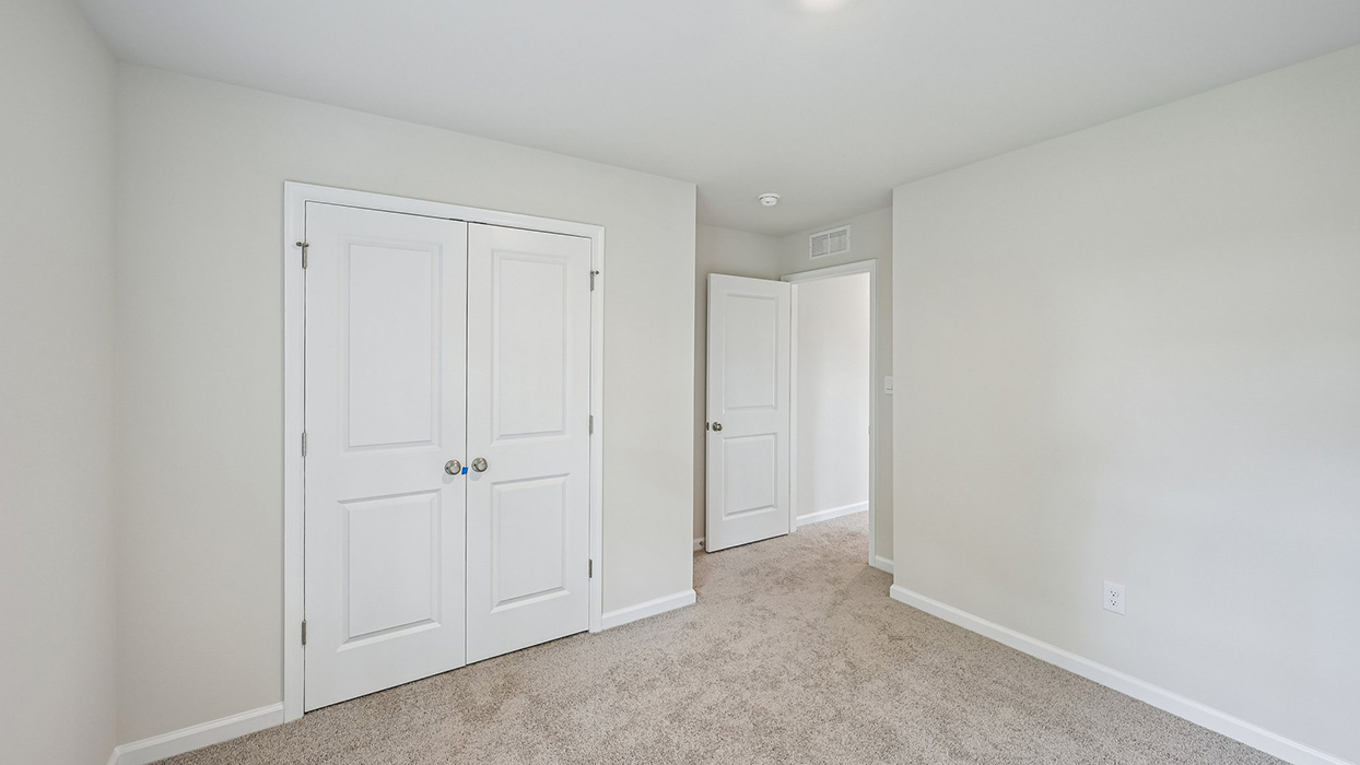 Secondary bedroom with double closet doors, carpet flooring, and open view to hallway