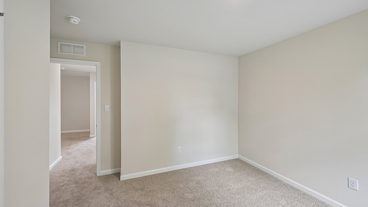 Bedroom with neutral carpet, partial wall detail, and doorway leading to hall