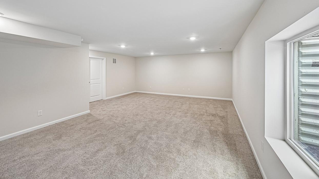 Basement living space with wide open layout, recessed lighting, and wall window detail