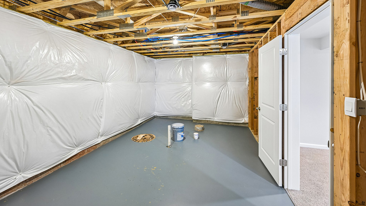 Unfinished basement storage area with insulated walls, bathroom rough-in, and access door