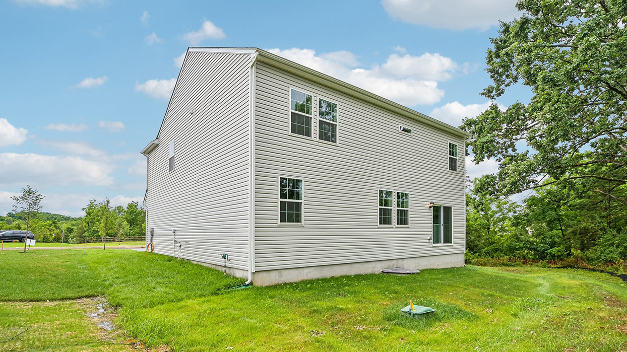 Rear side exterior featuring backyard lawn, multiple windows, and sliding glass door access
