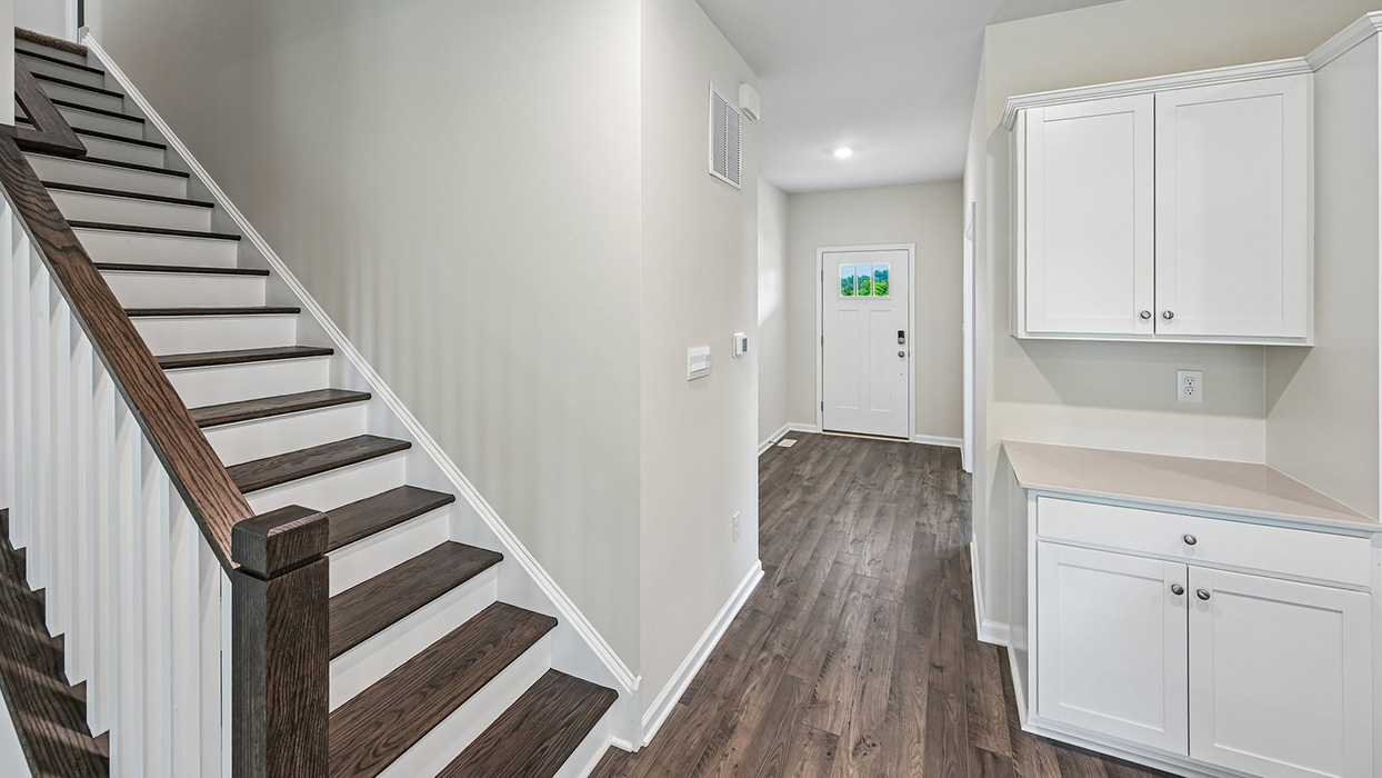 Staircase with stained wood treads and white railing alongside hallway and entry area