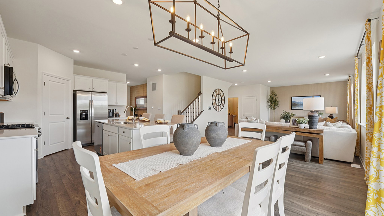 Dining space with a wooden table with a view towards the open-concept living pace and stairwell to the second floor.