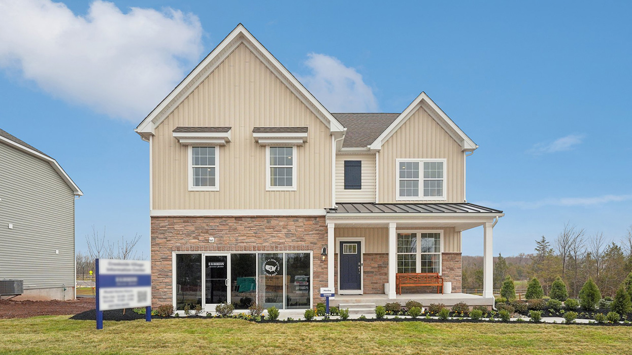Two-story home with a covered front porch, horizontal plank siding in complimentary colors of linen and navy with aspen ledgestone water-table accent, and a sales center front on the two-car garage.