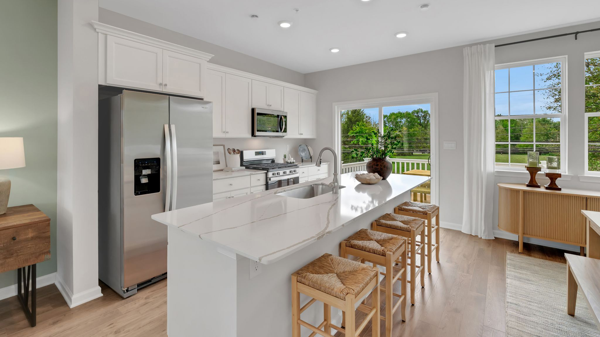 Kitchen area with large island and white marble counter tops and white cabinetry.