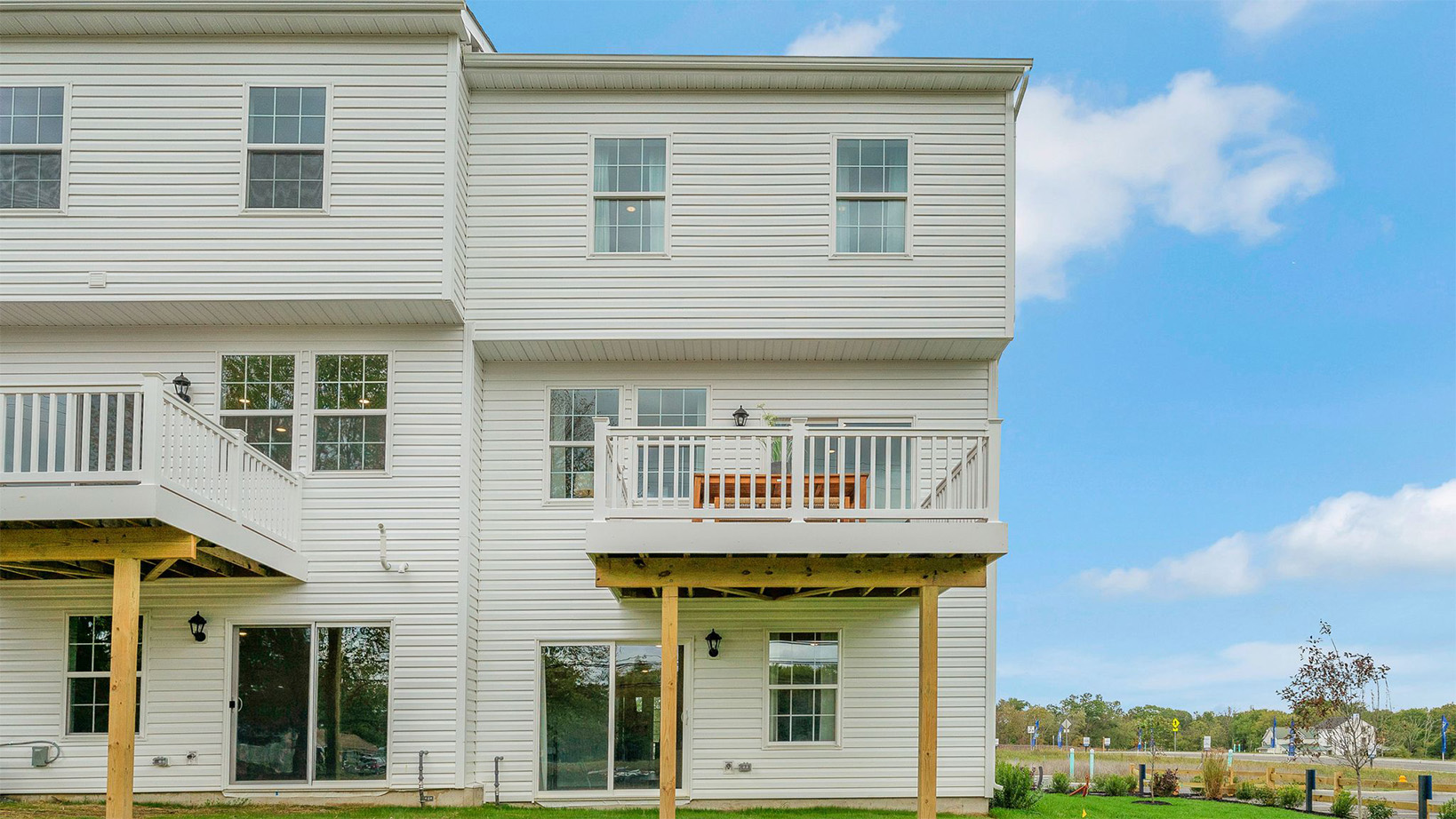 Exterior back image of a three story townhome with white horizontal paneling, the second story balcony, and the first floor back sliding glass door.