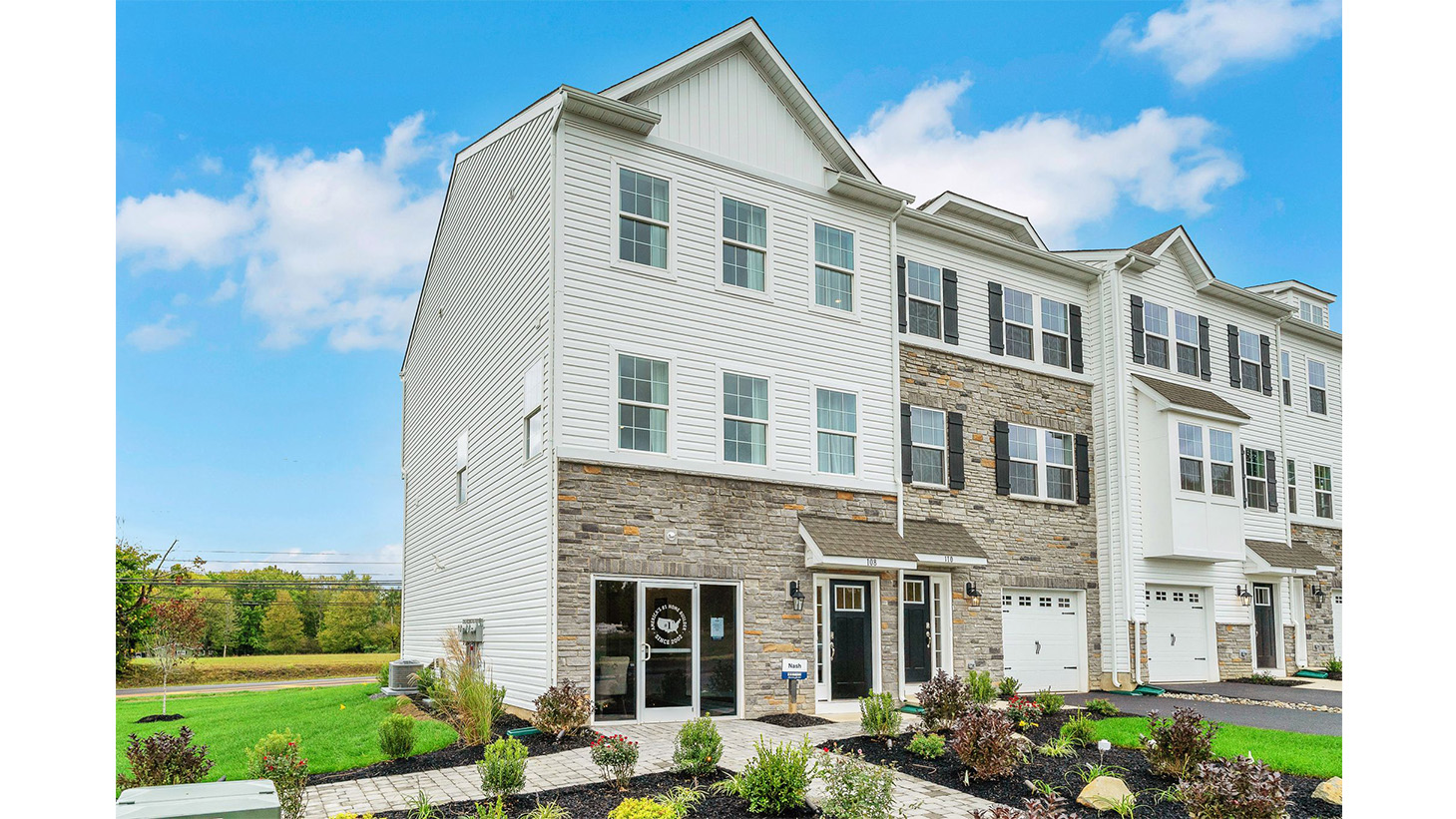 Exterior back image of a three story townhome with white horizontal paneling, the second story balcony, and the first floor back sliding glass door.