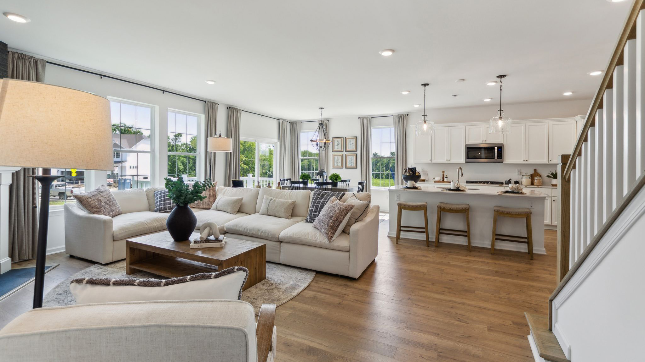 Open concept layout with stairs, kitchen, eating nook, and living area with windows encompassing the whole space.