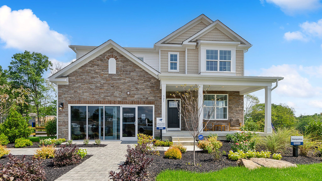 Exterior front image of the model home. Three story house with tan horizontal paneling and brick with a front porch.
