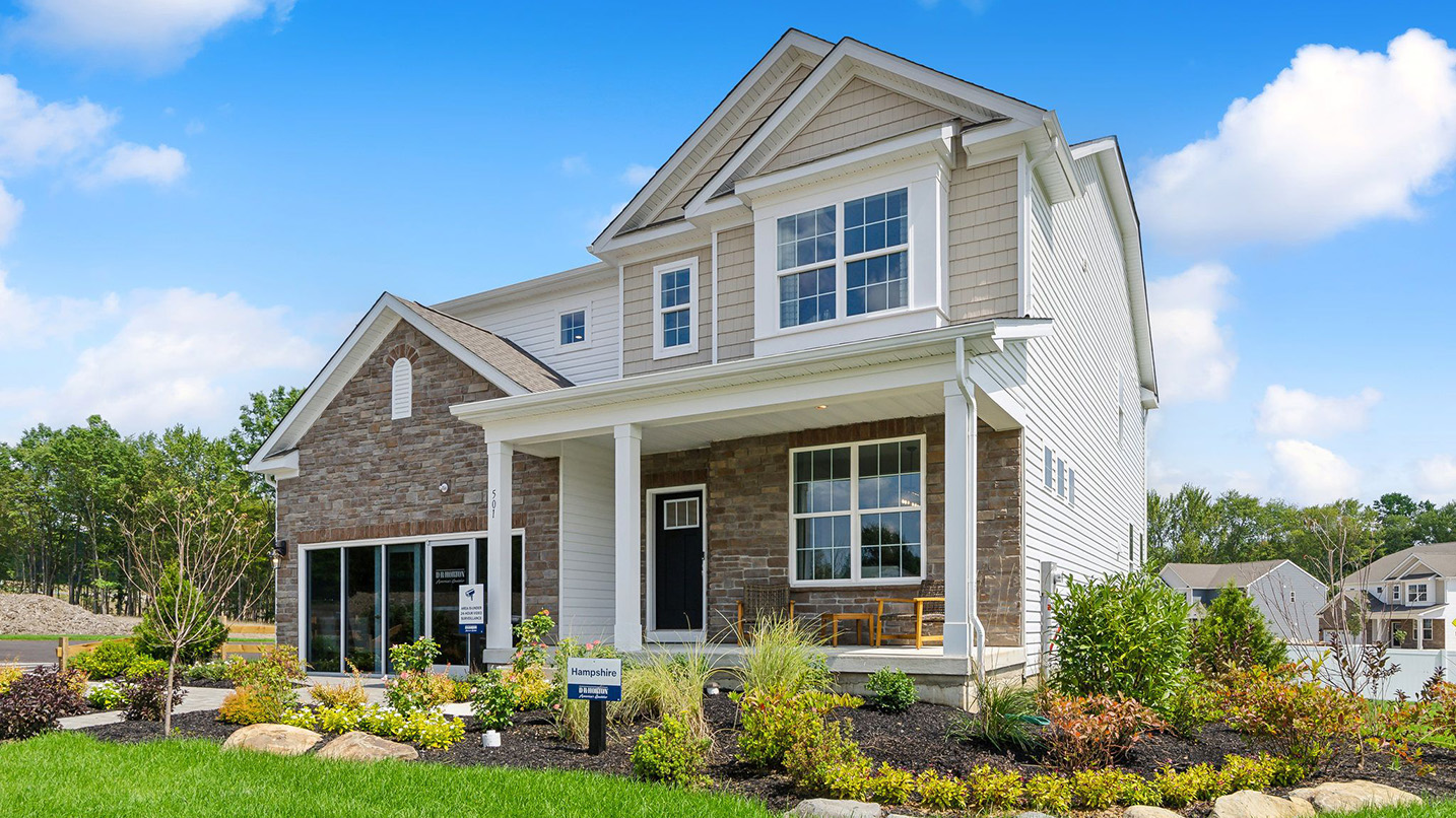 Exterior front image of the model home. Three story house with tan horizontal paneling and brick with a front porch.