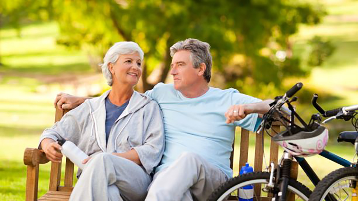 an older couple sitting on a bench with their bicycle nearby