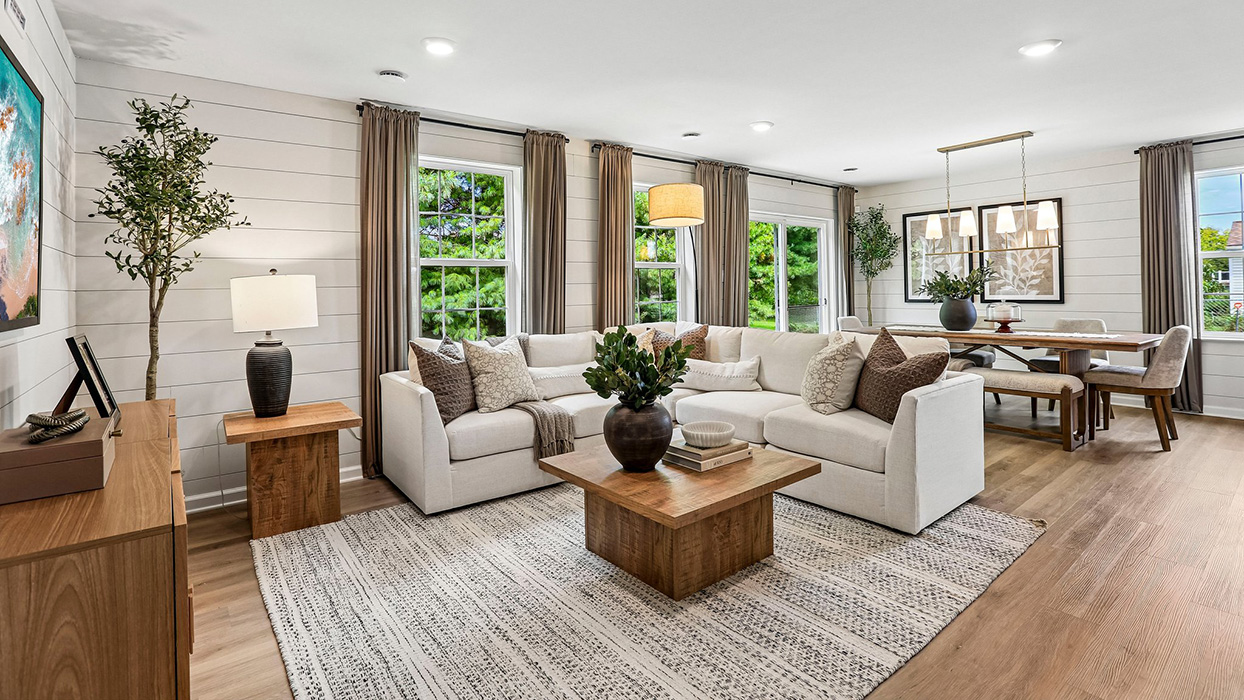 Open-concept living room with large windows, cozy seating, and abundant natural light in this inviting new home