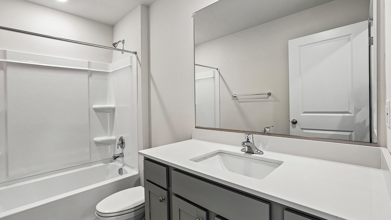 a secondary bathroom with gray cabinets and a shower tub