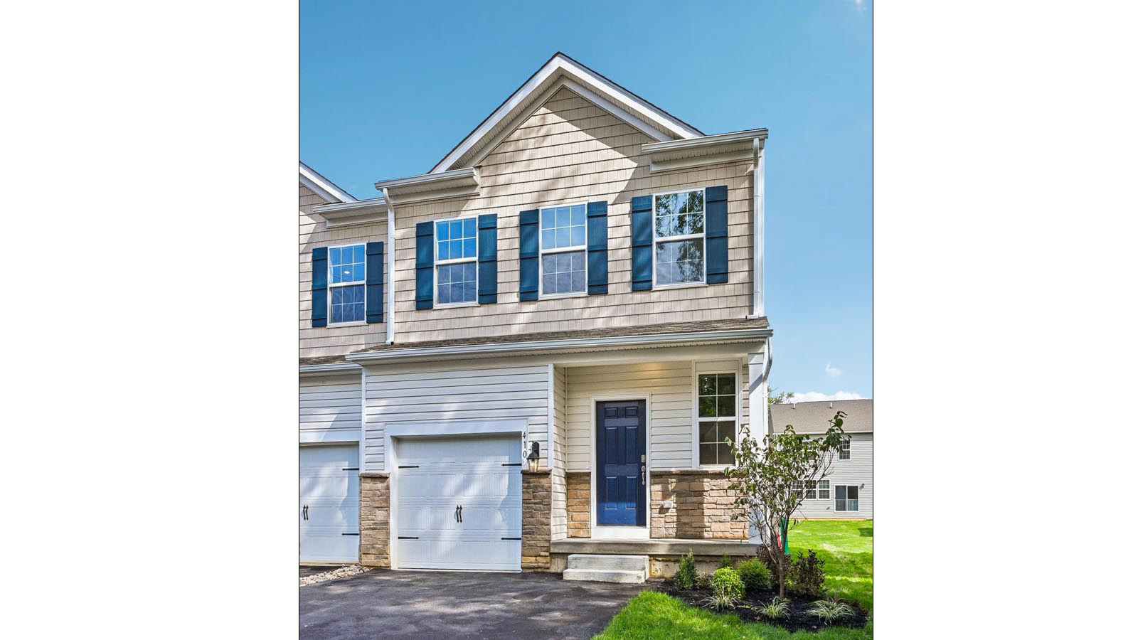 Wallingford Mews Charleston two story townhome with linen vertical and sand shake siding, aspen ledgestone kneewall, midnight blue shutters, and a white single car garage.