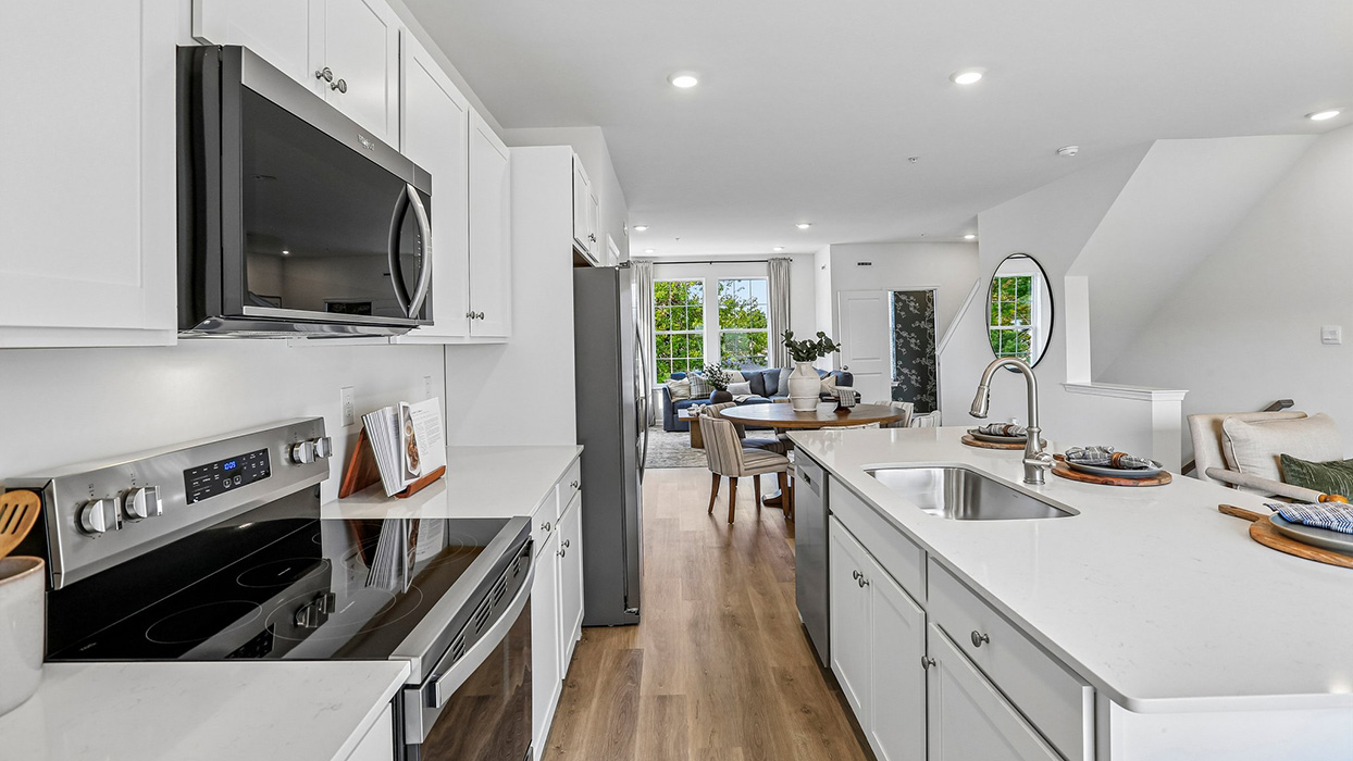 Bright spacious kitchen area with large island with white counter tops and white cabinetry and stainless steel appliances