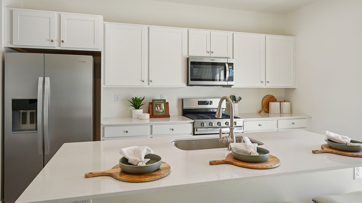 Kitchen island with white countertops and sink, paired with stainless steel refrigerator, stove, and microwave and ample cabinetry