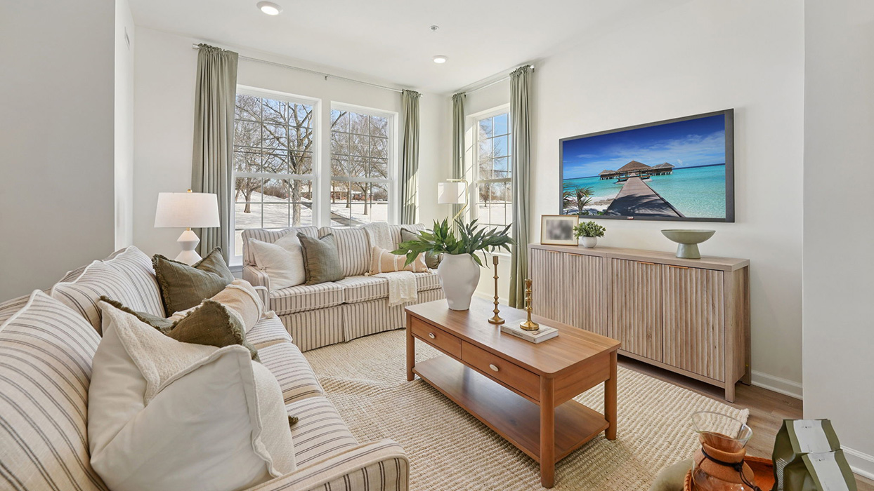 Living room with large sectional sofa, coffee table, and wall-mounted TV, surrounded by multiple windows with natural light