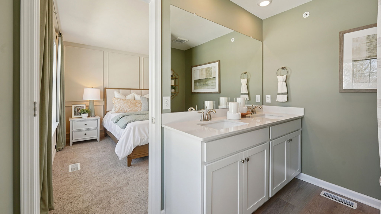 Primary bathroom with double sink vanity, large mirror, and view into adjacent bedroom