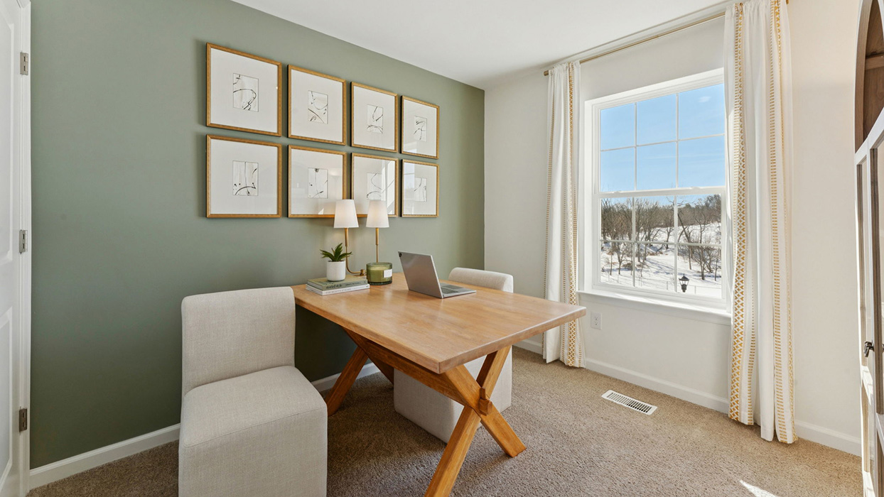 Home office with wood desk, accent wall art, and large window providing natural light
