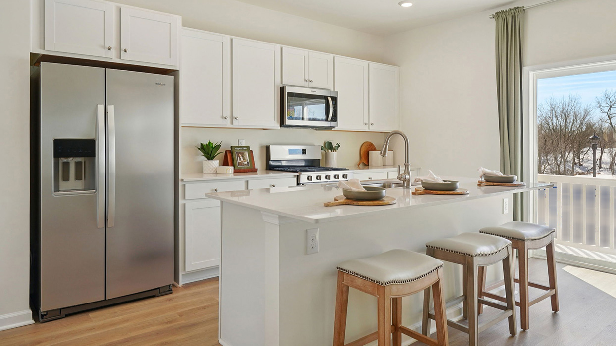 Kitchen with large island seating, white countertops, stainless steel appliances, and sliding glass door leading to a small deck