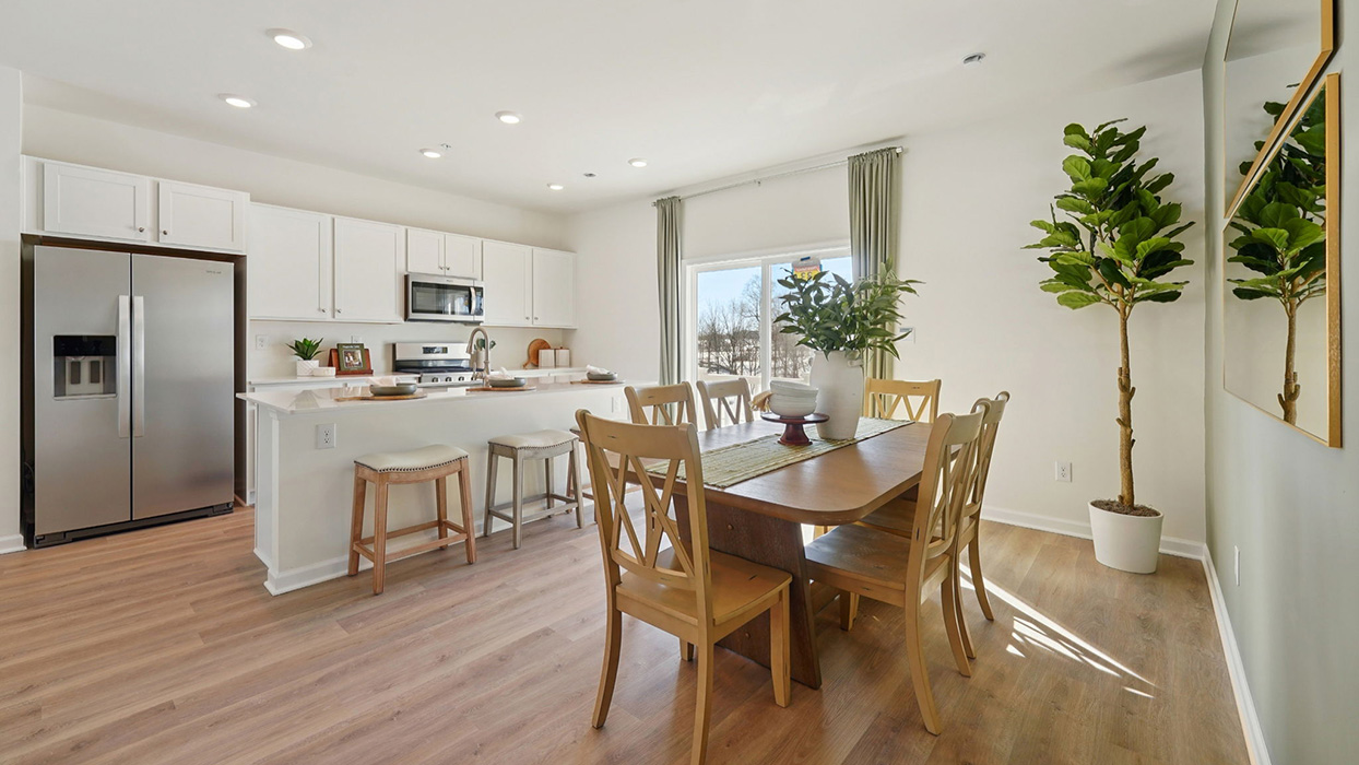 Dining area with wood table and chairs, adjacent to kitchen island, featuring sliding glass door and bright natural light