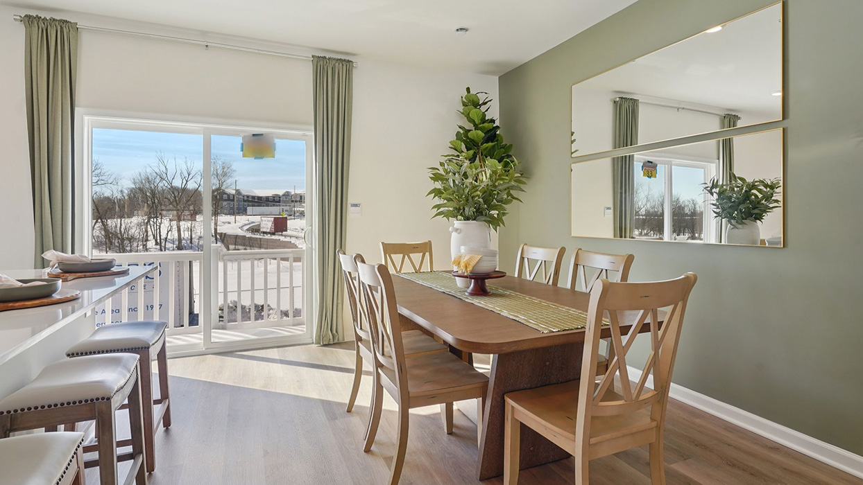 Dining area with wood table set against accent wall, large mirror, and sliding glass door bringing in natural light