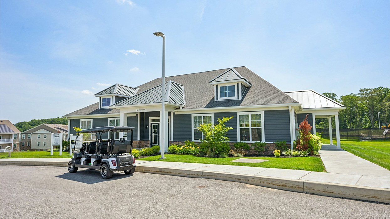 Clubhouse exterior at Enclave at Mi-Place with covered entry, stone accents, and golf cart parked along curbside drive